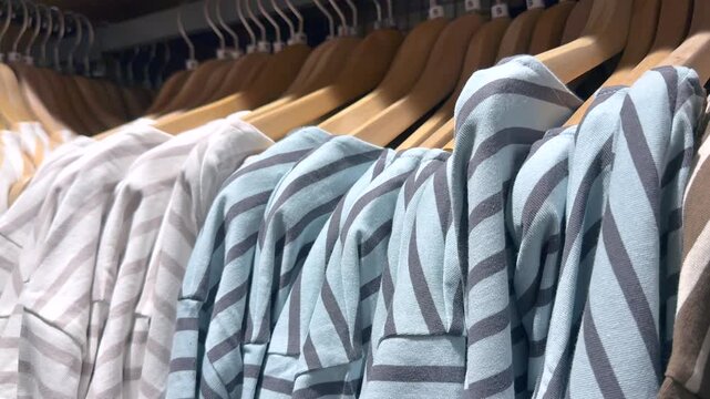Slow Pan Across Striped Shirts Hanging on Rack in Fashion Store. Fashion retail display with shallow depth of field and soft lighting. Ideal for shopping, apparel, boutique, and lifestyle concepts.
