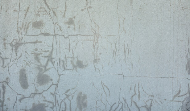 A close-up shot of an old textured concrete wall with multiple cracks and water stains over the surface