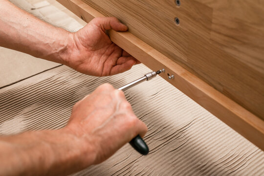 Hands tighten a screwdriver on a wooden furniture panel. Close up of manual assembly and repair work. Home improvement, DIY, and joinery task..