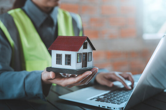 Property valuation construction cost estimation concept, mortgage planning, real estate developer, building investment, engineer holding miniature model house typing laptop computer working
