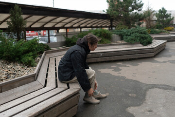 Obraz premium A person is sitting on a wooden bench, looking down at their shoes in an outdoor space