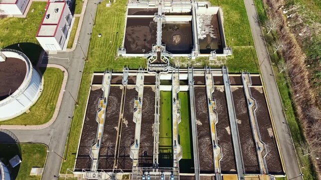 Workers manage equipment at a wastewater treatment location. Tanks hold materials while pipes carry waste for treatment in the complex. The setting is clear and well-organized.