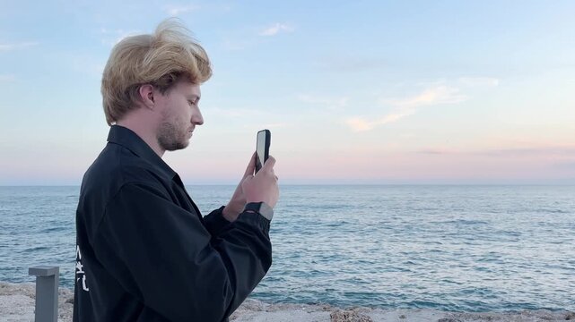 young man walking along the promenade and taking pictures.uses a smartphone