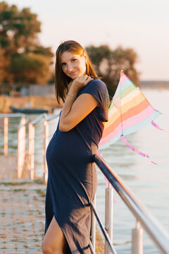 Smiling Pregnant Woman Holding Kite By The Rail