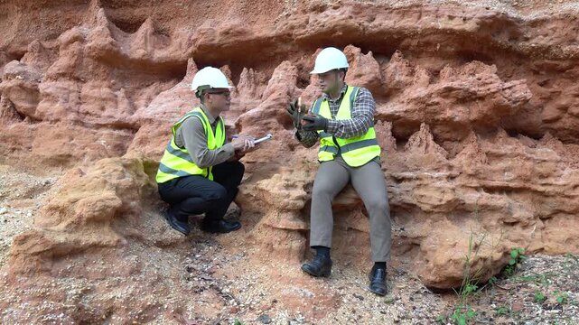 Two geologists analyzing soil and rock formations at a mining excavation site. They are conducting geological surveys and evaluating mineral resources for industrial project planning.