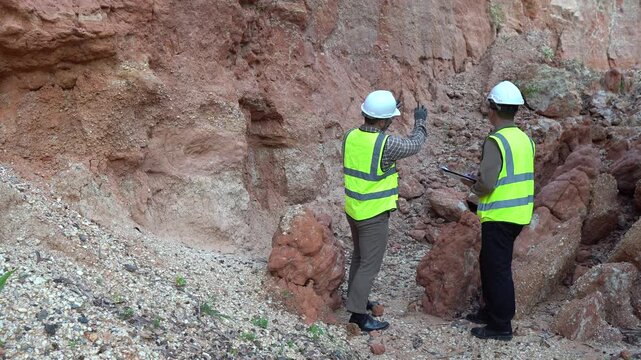 Two geologists analyzing soil and rock formations at a mining excavation site. They are conducting geological surveys and evaluating mineral resources for industrial project planning.