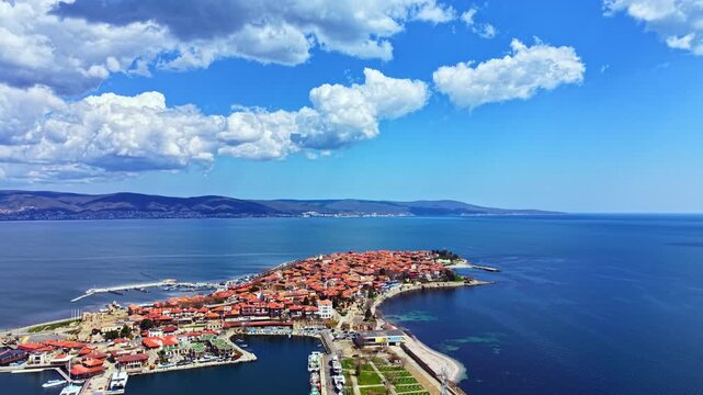 People enjoy their time in Nesebar Old Town, taking in the views and walking along the waterfront. The sea reflects the sky as boats are seen in the harbor.