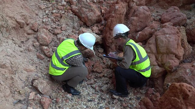 Two geologists analyzing soil and rock formations at a mining excavation site. They are conducting geological surveys and evaluating mineral resources for industrial project planning.