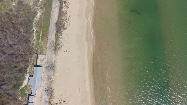 Aerial coastal scenery with rolling ocean waves and green water beside sandy beach shoreline nearby