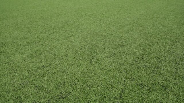 Slow camera movement across a flat artificial football pitch surface. Close view of green synthetic turf with visible texture, highlighting the even field and sports infrastructure under daylight.