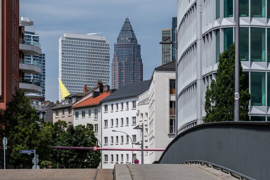 A quiet street foreground leads toward rooftops and skyline towers in Frankfurt Germany, placing urban district buildings within city architecture