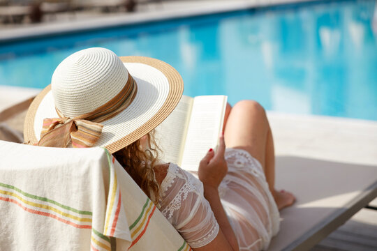 Woman reading book by poolside relaxing during summer vacation