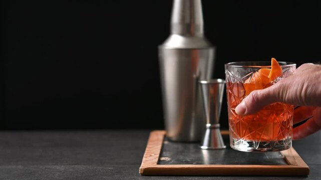 Hand Picking Up an Old Fashioned Cocktail Against Black Background