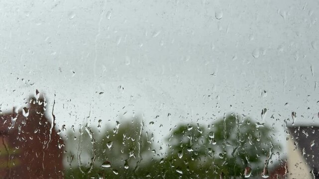 Raindrops falling on window on a cloudy windy day 4k background building and trees bokeh