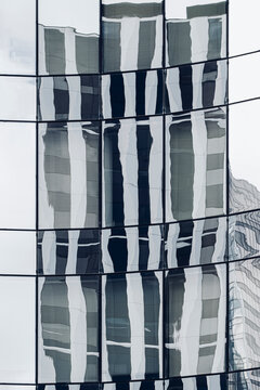 Wavy reflections distort office buildings across a glass facade as windows turn corporate architecture patterns into abstract vertical lines
