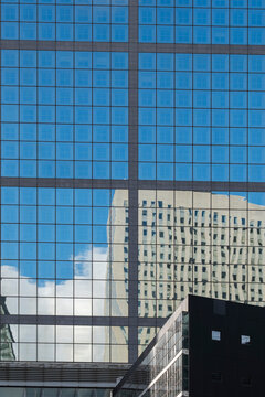 Clear reflections of office buildings align inside a glass facade where windows and corporate architecture create abstract patterns against sky