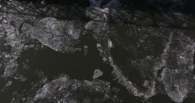 Aerial view of large ice floes floating on dark river water with a bridge shadow across the surface in Cincinnati, Ohio, United States.