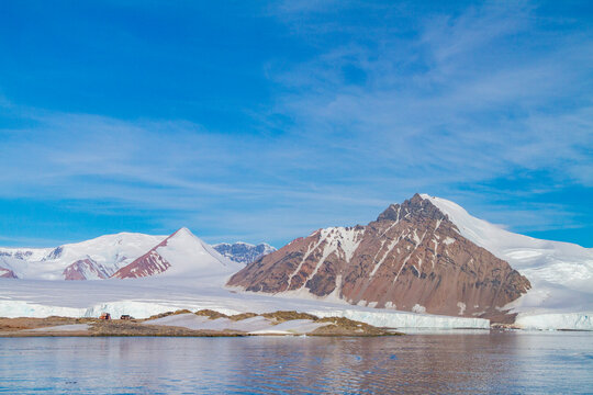 Research base on Stonington Island in Antarctica overlooks melting glaciers and rugged mountains under blue sky