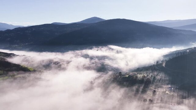 Aerial view of the village of Avo partially hidden by a thick blanket of morning fog in a valley surrounded by rolling hills and mountains Oliveira do Hospital, Coimbra District, Portugal.