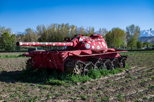 Old Russian tank stands in a field surrounded by trees and mountains in Afghanistan