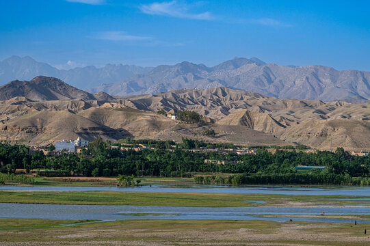 Overlook of the Kabul river showing distant mountains and green fields near Jalalabad in bright daylight with clear sky