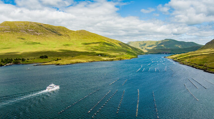 Fototapeta premium A tour boat cruises along Killary Fjord beneath bright green mountains and open skies in western Ireland. A scenic travel landscape highlighting sightseeing on Irelands only fjord.