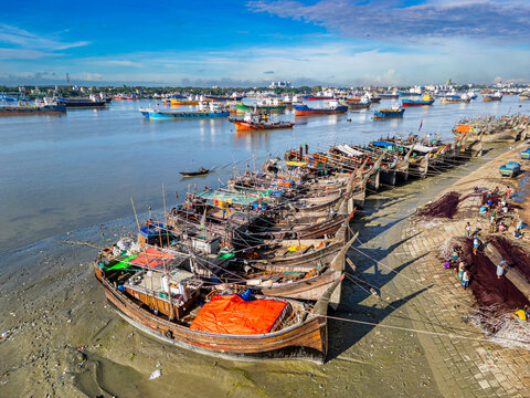 Boats anchor along the Karnaphuli River with fish market activity in Chittagong, Bangladesh on a clear day