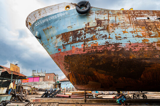 Men repair a boat in a shipwreck yard in Dhaka, Bangladesh during a cloudy day of work