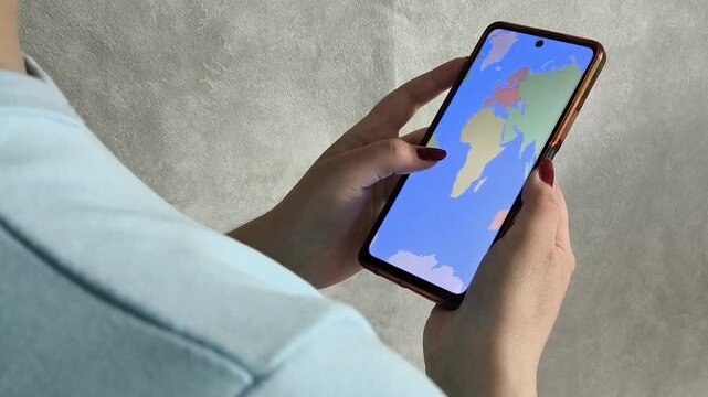 Map of the world on the phone screen in the hands of a woman, a view from over the shoulder. A woman chooses a place for a summer vacation, a vacation abroad