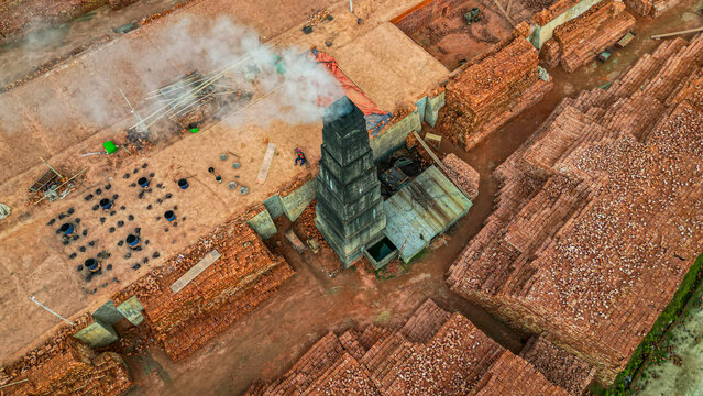 Brick production process taking place at a factory with stacked bricks and a chimney in Bangladesh