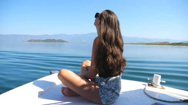Young girl sitting on bow of boat and floating through calm surface of sea bay. Unrecognizable woman enjoying beautiful nature landscape during summer travel. Concept of travel lifestyle. Slow mo