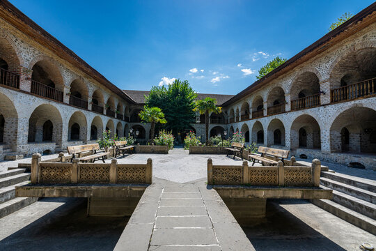 Visitors explore the Carawanserai, a UNESCO site in Sheki, Azerbaijan, featuring arches, gardens, and benches for rest and socializing