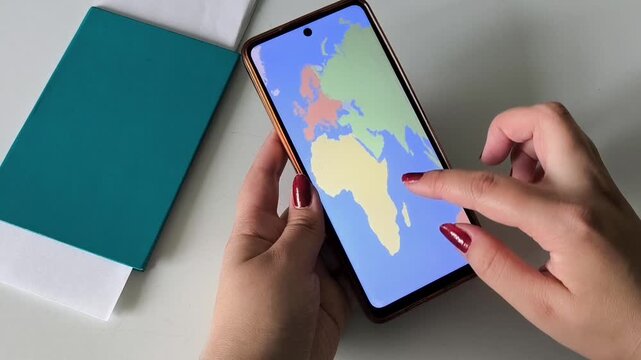 A map of the world on the phone screen in the hands of a woman, a passport and tickets on the table. Woman choosing a place for a summer vacation