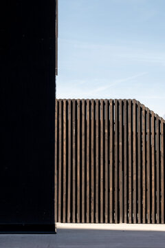 wooden slats run between black wall and pale sky as vertical rhythm shapes minimalist urban architecture on a quiet exterior facade
