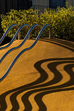 golden ramp curves under railings where sunlight projects shadows across urban playground surface and graphic architecture detail outside