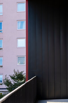 pink building appears beside black facade as stair railing cuts through shadow toward urban apartments and geometric architecture detail