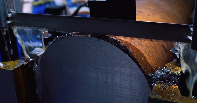 Metalworking. Modern industrial equipment.
A band saw, cooled by a special liquid lubricant, carefully cuts a large metal part. The technological process is filmed close-up.
