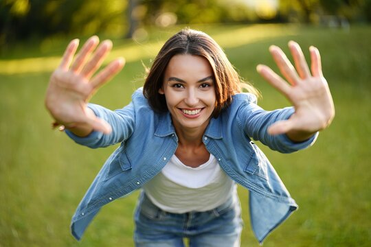 Smiling young woman with open arms in a green park during golden hour. Concept of freedom, happiness, carefree lifestyle and positive emotions.
