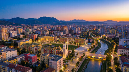 Fototapeta premium Panoramic aerial view of Tirana city skyline at dusk with a river flowing through the urban landscape.