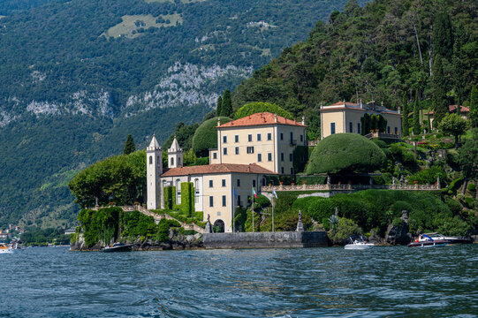 Villa del Balbianello sits by the shore of Lake Como with green hills in the background and boats in the water