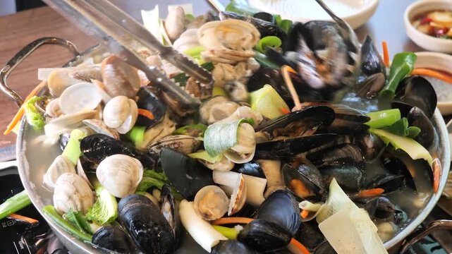 Pot containing oyster kalguksu topped with fresh seafood and vegetables