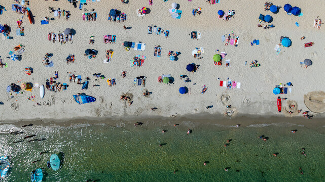 Crowds enjoy a sunny day at Legenese cove beach in Carnac, Brittany, France with umbrellas and activities on the sand