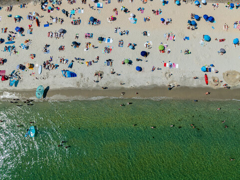 People enjoy a sunny day on Legenese cove beach in Carnac, Brittany, with umbrellas and water activities taking place