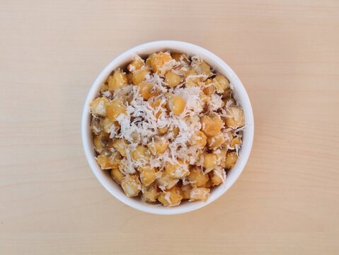 Urab Jagung or traditional indonesian sweet and savory snack made from boiled corn kernels mixed with fresh grated coconut, served in a clean white ceramic bowl on a wooden background