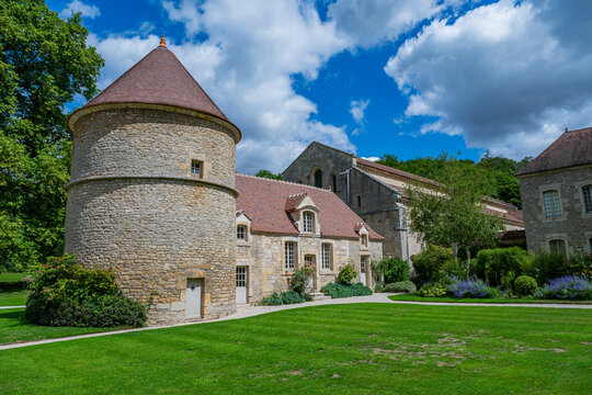 Abbey of Fontenay features round tower and stone buildings in green landscape with clouds above in France