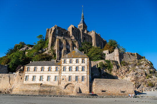 Visitors explore the base of Mont St. Michel in France while admiring its historic architecture and landscape under clear skies