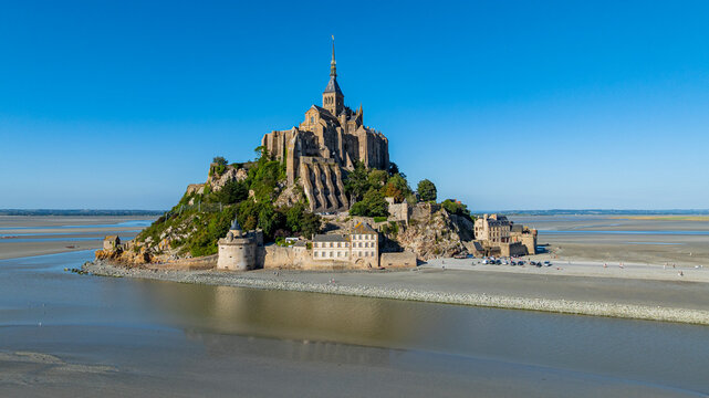 Aerial view showcases Mont St. Michel on a sunny day in the bay area of France with historic architecture and surrounding water