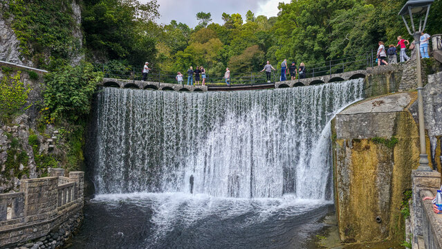 Visitors enjoy the view of the artificial waterfall while walking along the paved path in New Athon, Abkhazia during a sunny day