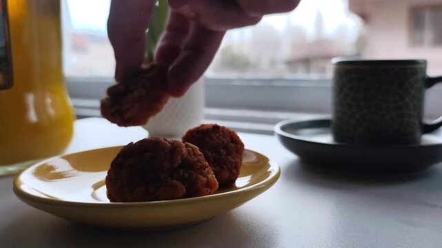 Static close-up shot of a hand placing crispy golden fried chicken nuggets one by one onto a small yellow saucer on a white table