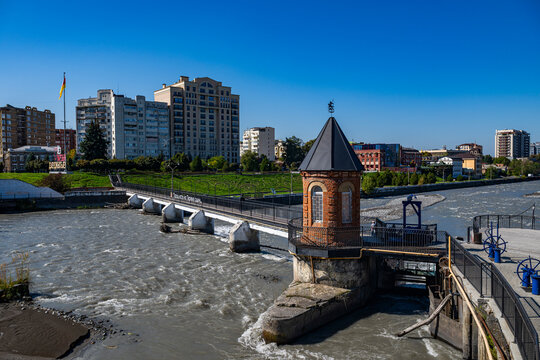 Little bridge spans Terek river near city buildings in Vladikavkaz, North Ossetia, Russia, on a clear sunny day